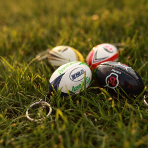 4 różne breloczki imitujące piłki sportowe leżące na trawie