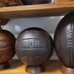 3 piłki retro na podstawkach drewnianych ustawione pa półce na regale