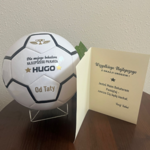Piłka nożna z napisem hugo na prezent, obok piłki stoi kartka z życzenami